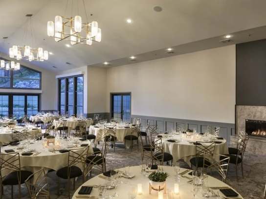 A modern ballroom set for a reception with round tables, gold chairs, and a fireplace.