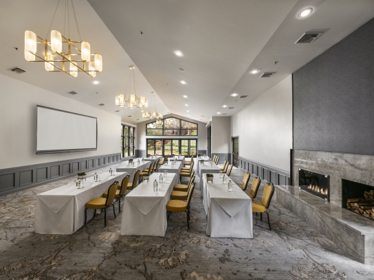 A modern ballroom in a classroom setup with long tables, a projection screen, and a large marble fireplace.