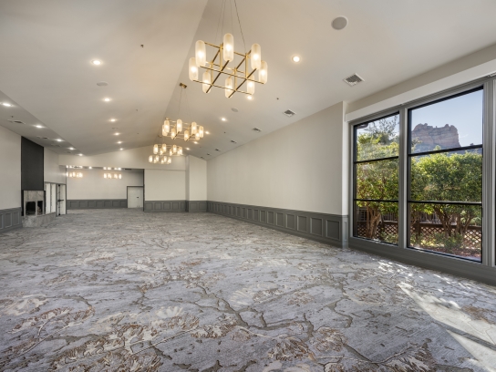 An empty, modern ballroom with patterned carpet, gold chandeliers, and a large window showing Sedona's red rocks.